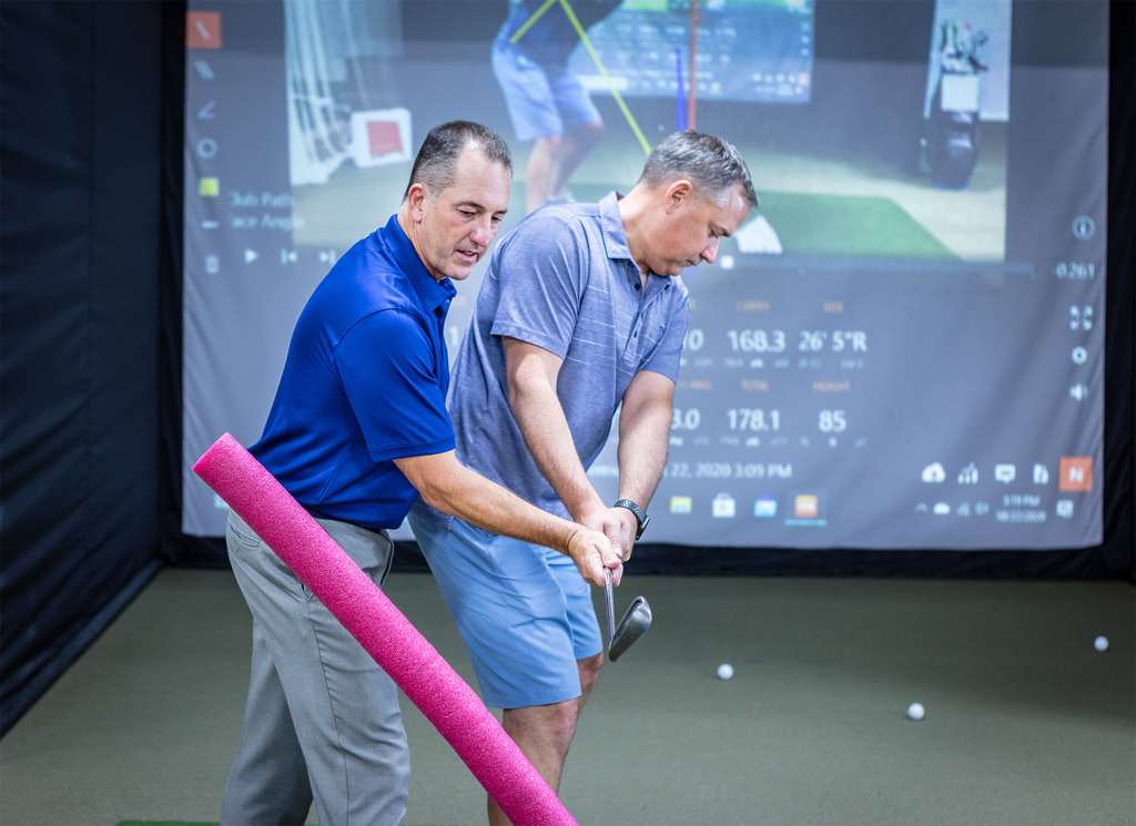 Golf instructor coaching student at indoor simulator