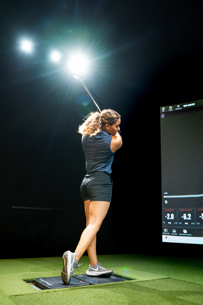 Woman golfer swinging club in indoor simulator